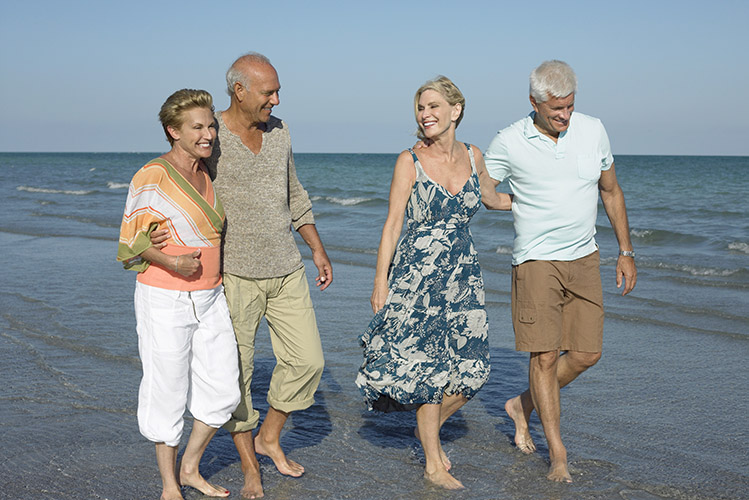 Two senior couples walking barefoot on beach
