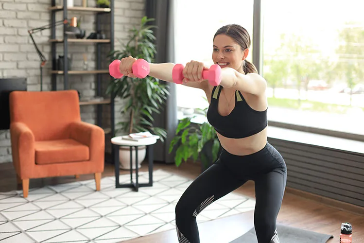 Beautiful slim fitness woman crouches with dumbbells