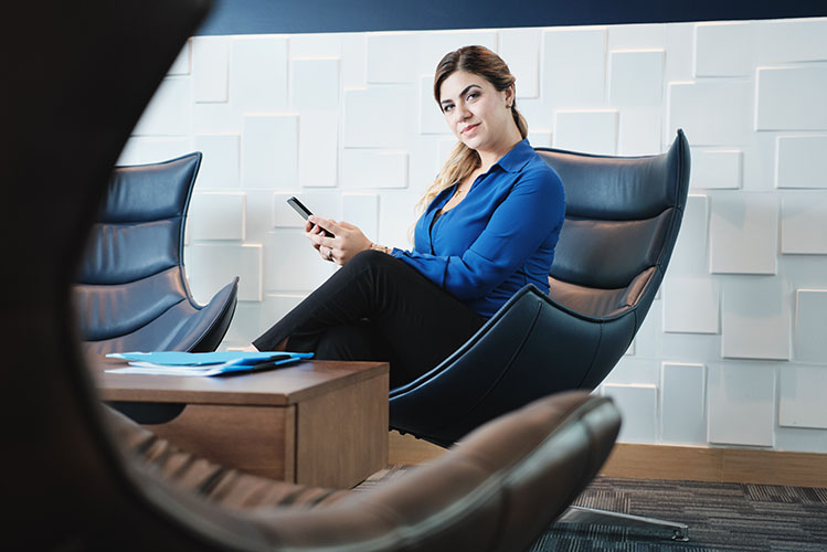 woman holding cell phone at work in office waiting room, sitting on armchair