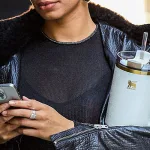 woman holding phone and travel mug