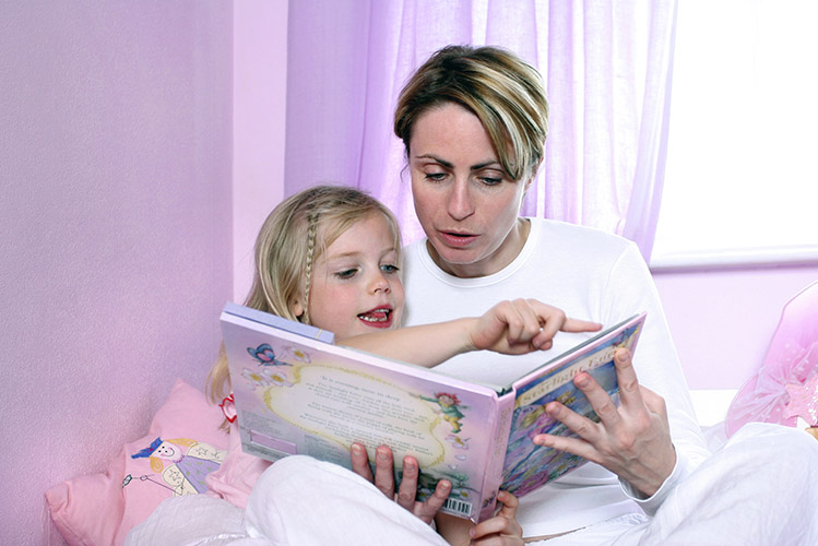 woman sitting on the bed reading bedtime story to little girl