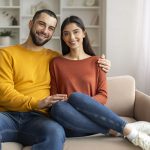Loving Young Couple Embracing While Sitting On Sofa At Home