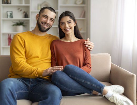 Loving Young Couple Embracing While Sitting On Sofa At Home